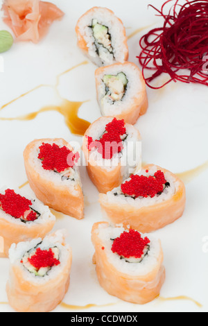 Eine Nahaufnahme mehrerer Sushi-Rollen, die auf einer weißen Oberfläche angeordnet sind. Die Brötchen werden in Lachs gewickelt und mit Reis, Gurke und anderen Zutaten gefüllt, garniert mit hellrotem Kaviar. Einige Rollen werden geschnitten Stockfoto