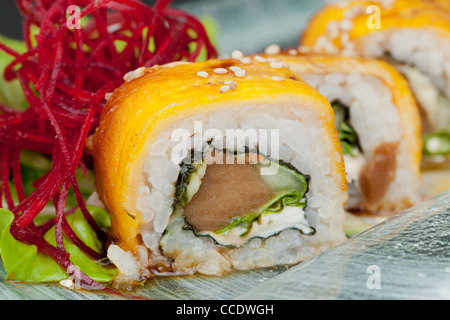 Eine Nahaufnahme einer in Scheiben geschnittenen Sushi-Rolle mit einer hellgelben Außenschicht, wahrscheinlich Tamago (süßes Ei), belegt mit weißen Sesamsamen. Der Querschnitt zeigt Schichten von weißem Reis, ein Stück davon Stockfoto