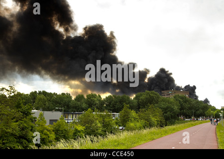 Schwarzer Rauch aus der Verbrennung von Kautschuk gehen über die Stadt - in einem großen Feuer einer Recyclingfabrik brannte zu Boden Stockfoto