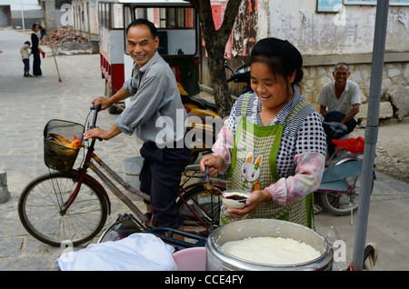 Lachen Mann mit Leben Hühner im Fahrradkorb und Straßenhändler verkaufen frischen Quark behandeln in Fuli Peoples Republic Of China Stockfoto