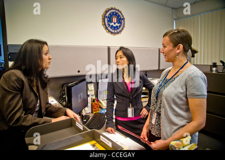 Drei weibliche FBI-Agenten diskutieren einen Fall in Santa Ana, CA, Büro. Beachten Sie Filipino-Amerikaner im Zentrum und FBI Logo auf Wand. VERÖFFENTLICHT Stockfoto