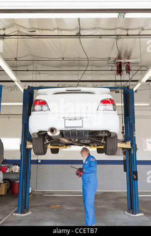 Mechaniker überprüfen unter Wagen auf einer Hebebühne Stockfoto