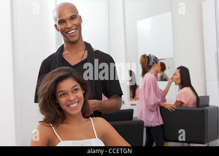 Junge Frau auf Stuhl sitzend mit Friseur hinter Stockfoto