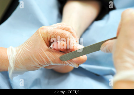 Eine Fußpflegerin behandelt ein Patient Fuß durch Feilen der Zehennägel. Stockfoto