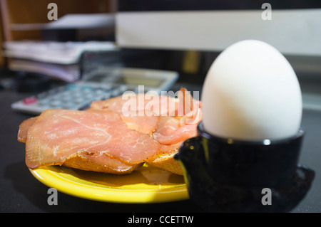 Frühstück mit geräuchertem Schinkenbrot Brötchen und gekochtes Ei am Computerschreibtisch von einem home-office Stockfoto