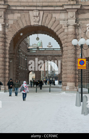 Touristen und Einwohner von Stockholm Fuß durch einen steinernen Torbogen in der Nähe des Königspalastes in den Schnee. Stockfoto