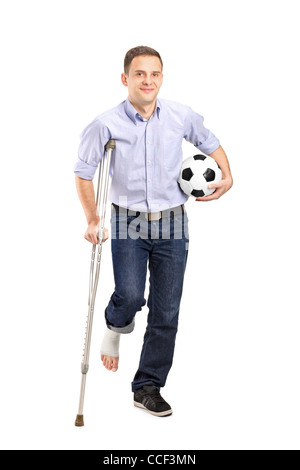 In voller Länge Portrait von einem verletzten jungen Mann auf Krücken hält einen Fußball isoliert auf weißem Hintergrund Stockfoto