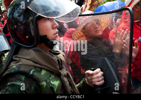 27. März 2010 schaut - Bangkok, Thailand - Anti-Regierungs-Demonstranten durch die Abschirmung der Thai Soldat im anti-Riot gear wie sie ebnen den Weg durch Anti-Regierungs-Demonstranten beim Verlassen des Zoogeländes des buddhistischen Tempels in Nähe der Regierungsgebäude. Anti-Regierungs-Demonstranten wurden chee Stockfoto