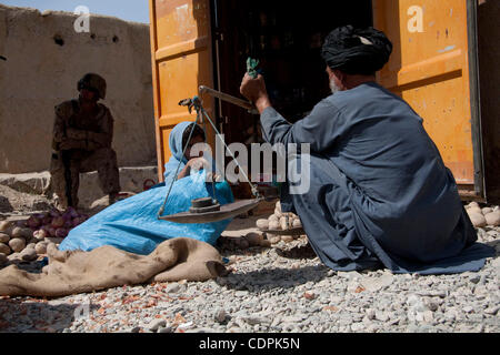 27. April 2011 - Stadt des Naw Zad, Naw Zad District, Helmand, Afghanistan - ein lokalen Anbieter wiegt Kartoffeln auf einer provisorischen Skala mit Hilfe seiner Tochter als eine eine Marine von Lima Company, 3. Bataillon des 2. Marineregiment bleibt im Hintergrund während einer gemeinsamen Patrouille mit ANA-Soldaten in den Bazar Stockfoto