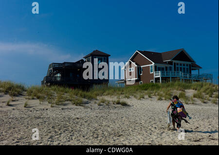 28. Juni 2011 - Frisco, North Carolina, Vereinigte Staaten von Amerika - A Frau Blätter am Strand, mit Stühlen, ein Handtuch und ein Regenschirm spazieren auf den Sanddünen in Richtung ihrer Sommer-Strand Haus in den Outer Banks von North Carolina, ist eine Sammlung von Barriere-Inseln erstreckt sich über 100 Meilen ein Stockfoto