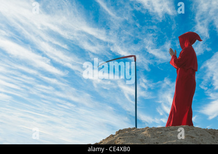 Unheimliche Figur im roten Mantel mit Sense Stockfoto