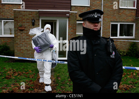 Szene des Verbrechens Offiziere Entfernen eines Computers aus einem Tatort, wie ein Polizist Wache steht. Bild von James Boardman. Stockfoto