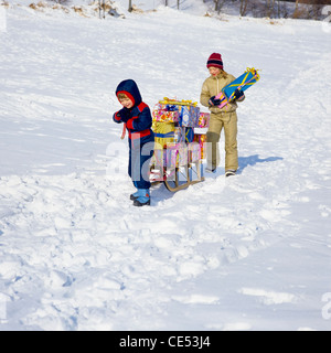 Kleiner Junge zieht einen Schlitten mit Geschenken beladen, Mädchen zu Fuß hinter; Schnee, Elsass, Frankreich, Europa Stockfoto