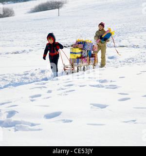 Kleiner Junge zieht einen Schlitten mit Geschenken beladen, Mädchen zu Fuß hinter; Schnee, Elsass, Frankreich, Europa Stockfoto