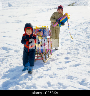 Kleiner Junge zieht einen Schlitten mit Geschenken beladen, Mädchen zu Fuß hinter; Schnee, Elsass, Frankreich, Europa Stockfoto