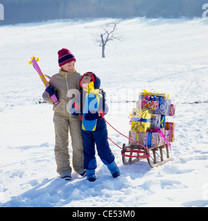 Junge und Mädchen mit Schlitten beladen mit Geschenken, Schnee, Elsass, Frankreich, Europa Stockfoto