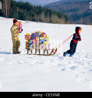 Kleiner Junge zieht einen Schlitten mit Geschenken beladen, Mädchen zu Fuß hinter; Schnee, Elsass, Frankreich, Europa Stockfoto