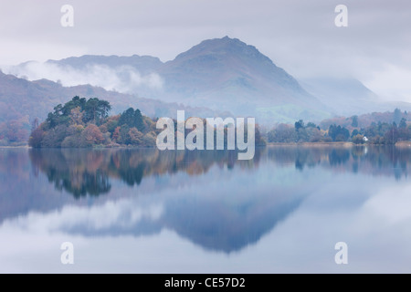 Nebel hängt über den See und die Insel in Grasmere mit Helm Crag hinaus Seenplatte, Cumbria, England. Herbst (November) 2011. Stockfoto