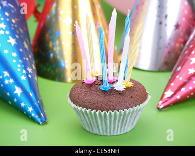 Schoko-Muffin dekoriert mit acht Kerzen mit Partei Konusklappen im Hintergrund Stockfoto