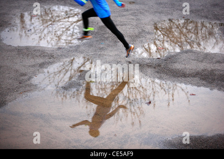 2 junge Frauen im Winter laufen, nasse springen über Flecken auf dem Weg. Stockfoto