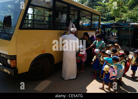 Viele kleine Kindergarten Kinder im Schulbus und Lehrer helfen ihnen, die Schritte im Schulbus zu klettern. Stockfoto