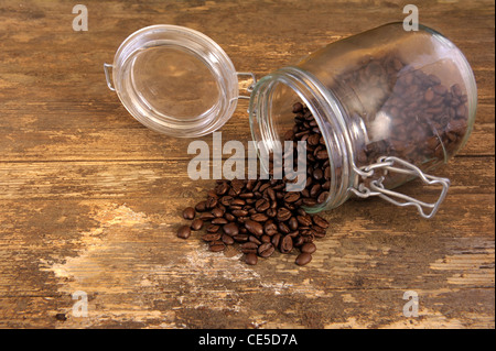 Kaffee Bohnen aus dem Glas in Glas auf eine alte verwitterte Tabelle verschütten Stockfoto