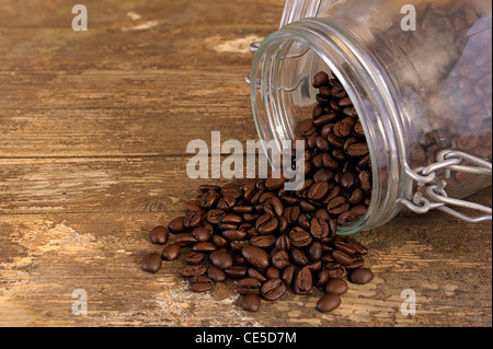 Kaffee Bohnen aus dem Glas in Glas auf eine alte verwitterte Tabelle verschütten Stockfoto