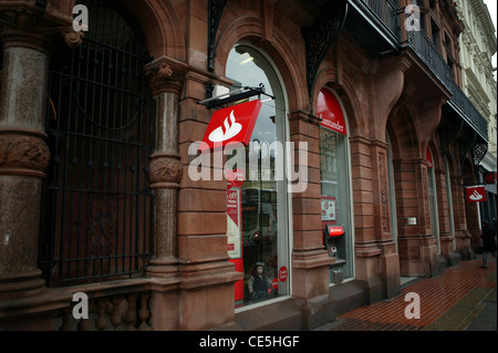 Santander Bank, Royal Avenue rot-weiße Logo, Sandsteinbau, geschnitzte Säulen. ATM, Bogenfenster. Schwarz Tore Stockfoto