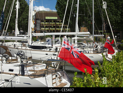 Red Ensign Fahnen auf Yachten ankern neben The Dickens Inn in St. Katharine Dock, London, England, UK. Stockfoto