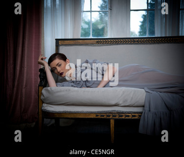 Eine Frau trägt eine langen graue Kleid, auf einem Sofa liegend Stockfoto