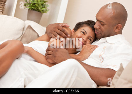 Glücklich afroamerikanische Mann und Frau Paar in den Dreißigern, die zu Hause sitzen, zusammen lachen und kuscheln Stockfoto