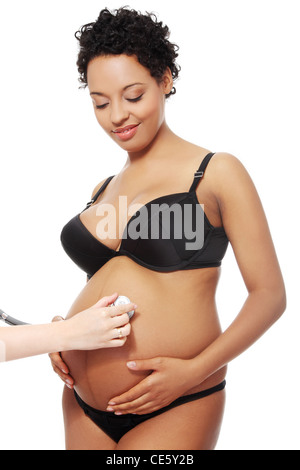 Vordere vierw Porträt einer jungen schönen Frau in ihrem Bauch mit einem Stethoskop, auf weißem Hintergrund isoliert untersucht. Stockfoto