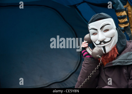 Ein Maskierter Demonstrant tragen Guy Fawkes Maske, bei St. Pauls lagerten London Website auf einem alten Telefon, Zelt im Hintergrund beschäftigen. Stockfoto