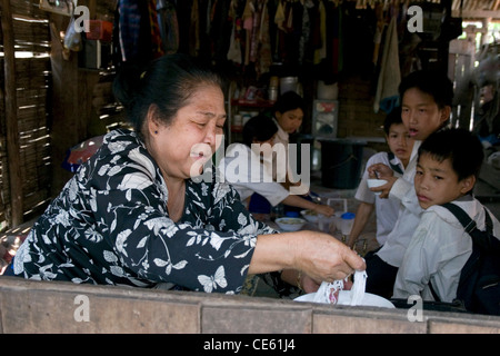 Eine asiatische Frau macht eine Schüssel mit Nudeln für Grundschulkinder in den ländlichen Dorf Ban Baumlao, Laos. Stockfoto