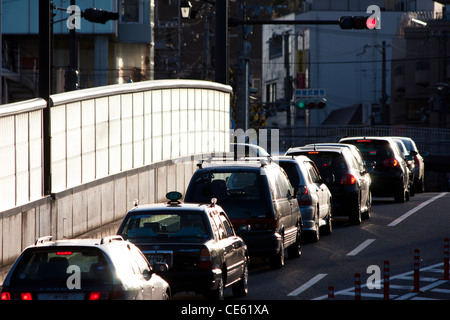 Kontrastreiche Ansicht entlang einer einzigen Linie von Autos, die an einer roten Überkopfstopleuchte auf der Yamate Kansen-Straße in Shukugawa, Nishinomiya, Japan, warten. Stockfoto