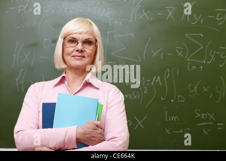 Porträt von Reife Lehrer mit Blick in die Kamera von Blackboard auf Hintergrund Heften Stockfoto