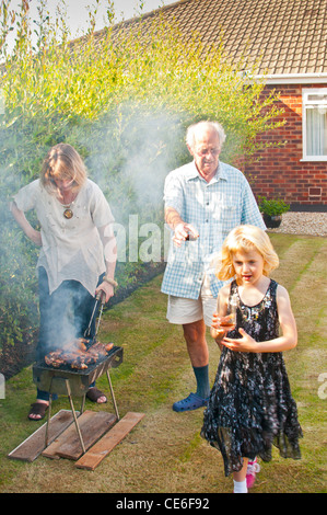 Familie Grill Garten Blackpool England uk Europa Kochen unter freiem Himmel Bbq Fleisch Rauch junge Frau smokey Rauch Augen Rauch in Augen Stockfoto