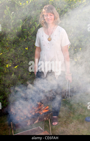 Familie Grill Garten Blackpool England uk Europa Kochen unter freiem Himmel Bbq Fleisch Rauch junge Frau smokey Rauch Augen Rauch in Augen Stockfoto