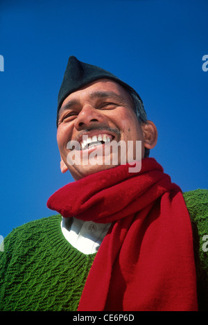 Mann lachend mit grünen Pullover rot Schal weißes Hemd schwarz Mütze gegen blauen Himmel Indien Herr #542 Stockfoto
