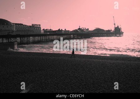 Einsame weibliche Gestalt, die zu Fuß am Strand in der Nähe von Brighton pier Stockfoto