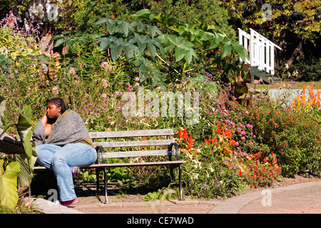 Afroamerikanische Frau sitzt auf einer Parkbank Stockfoto