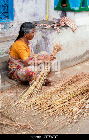 Indische Frau geschwungene Bürsten aus trockenen Gräsern Stiele machen. Andhra Pradesh, Indien Stockfoto