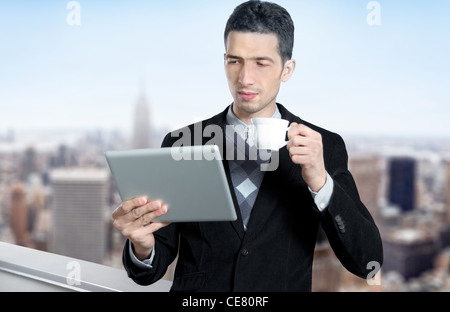 Junger Geschäftsmann mit einer Tasse Kaffee verwendet eine digitale-Tablette auf dem Dach des Business Centers. Verschwommene Stadtbild mit Wolkenkratzern Stockfoto