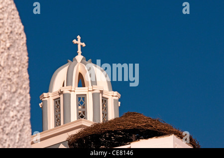 Kuppel der Kirche mit Kreuz in der Nähe von einem Strohdach Resort Regenschirm, Firostefani, Santorin, Griechenland Stockfoto