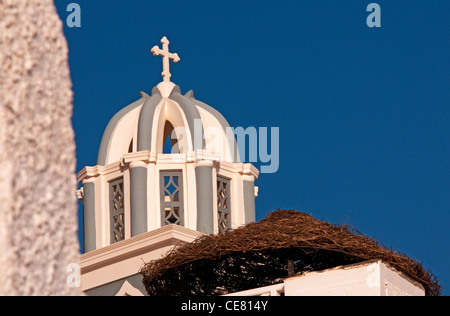 Kuppel der Kirche mit Kreuz in der Nähe von einem Strohdach Resort Regenschirm, Firostefani, Santorin, Griechenland Stockfoto