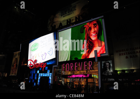 Nacht Sicht Menschen, Verkehr, Neon Fassaden LED Bildschirme, Disney Store, weibliche Modellbild Forever 21 Boutique, 7th Avenue, New York Stockfoto