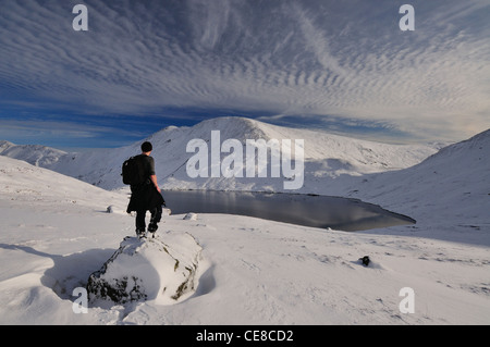 Walker mit Blick auf den Schnee bedeckt Seenplatte Landschaft. Grisedale Tarn und Fairfield an einem schönen Wintertag Stockfoto