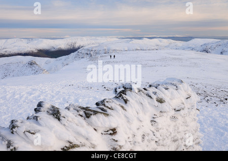 Käserand Schneewand des Tierheims Gipfel auf Lakelandpoeten mit zwei Wanderern in Richtung Striding Edge im Hintergrund Stockfoto