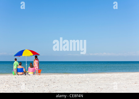 Rückansicht einer glücklichen Familie Eltern Tochter & Sohn Kinder Spaß im Liegestuhl unter einem Sonnenschirm an einem sonnigen Strand