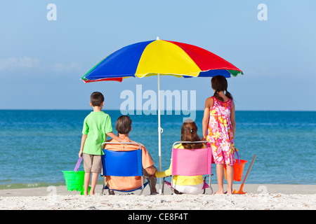 Rückansicht einer glücklichen Familie Eltern Tochter & Sohn Kinder Spaß im Liegestuhl unter einem Sonnenschirm an einem sonnigen Strand